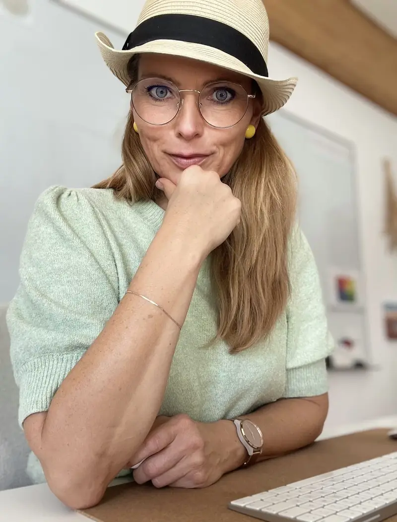 Kristin Fuchs mit Hut und Brille am Schreibtisch